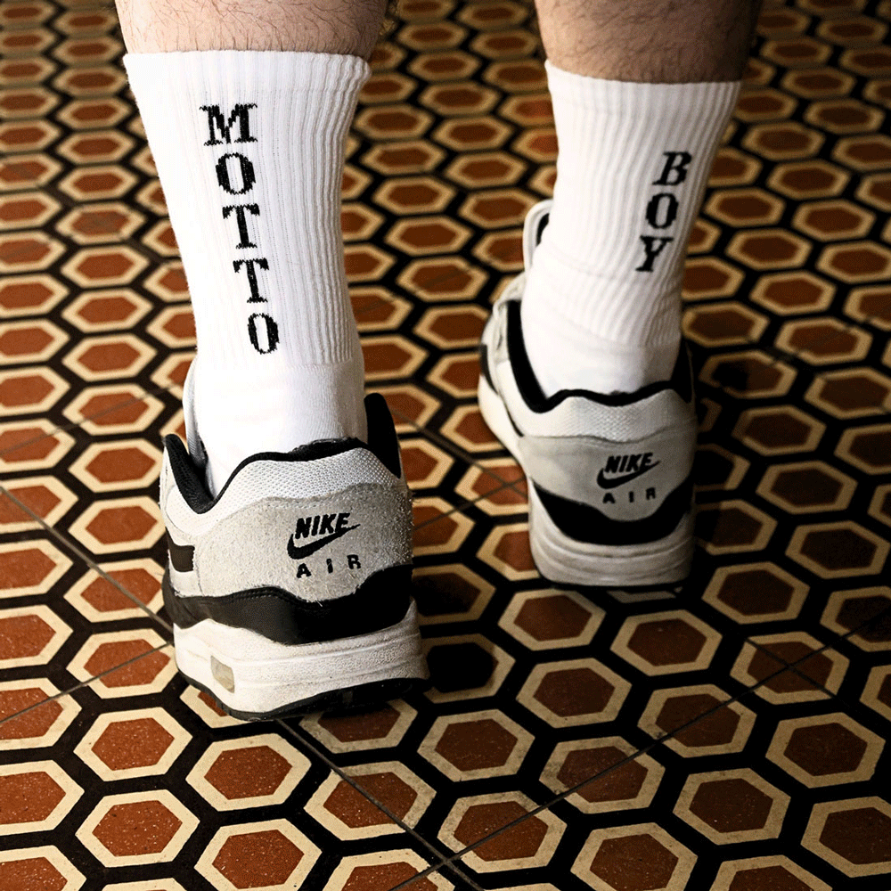 Füße in weißen Socken mit MOTTO und LOVE Schriftzug und weißen Turnschuhen auf gemustertem Boden bei Hotel Motto Wien