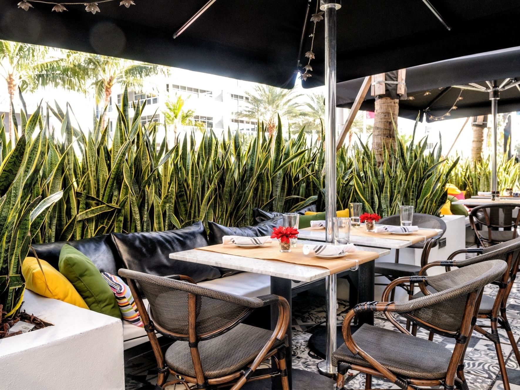 Outdoor dining area at The Tavern restaurant with umbrellas, tables, chairs, and plants near Tradewinds Apartment Hotel