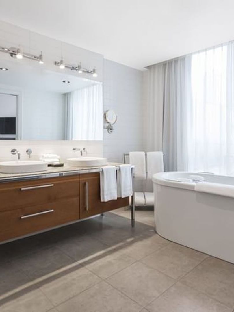 Penthouse René-Lévesque bathroom featuring a wood vanity with a mirror by the bathtub at Warwick Le Crystal Montreal