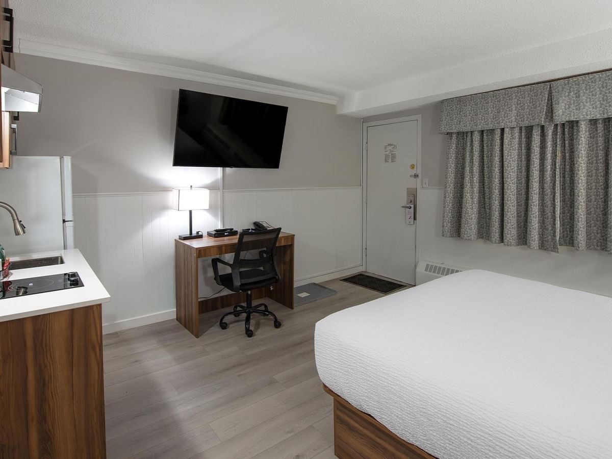 Room with Queen bed, kitchenette, work desk, and TV.