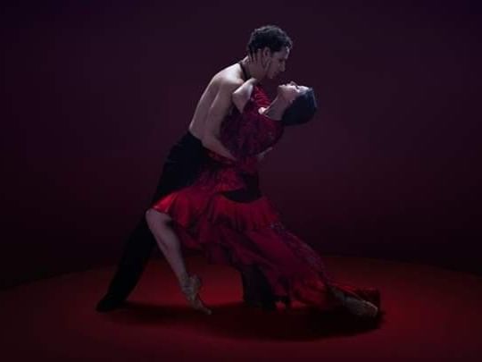 Two dancers passionately embracing during a performance on a dark red stage with dramatic lighting at The Sebel Brisbane