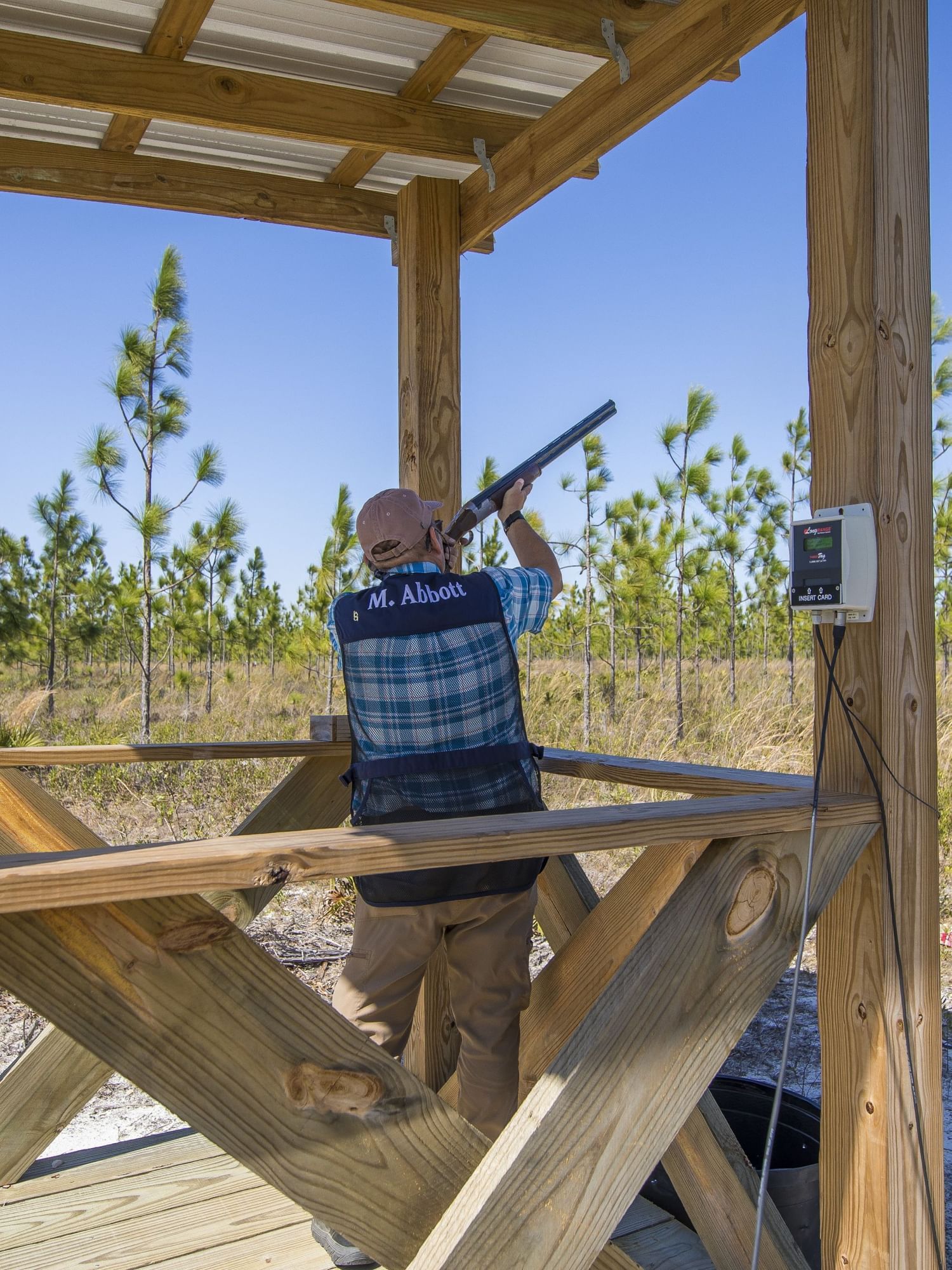 Man aiming a shotgun at a target from a raised wooden platform.