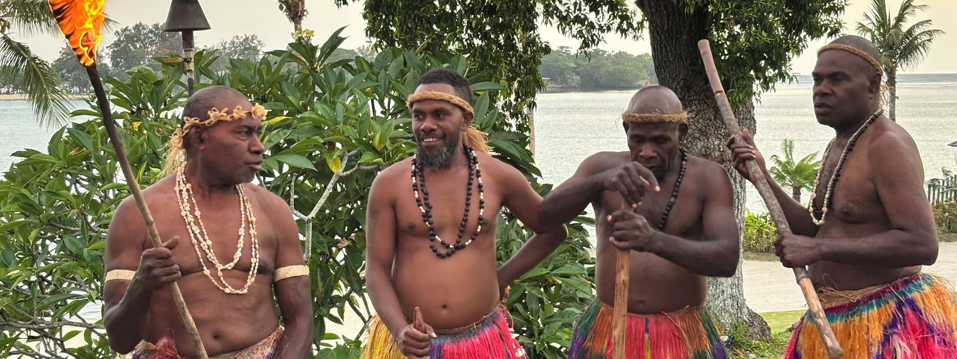 Four men in traditional attire holding torches and sticks at Warwick Le Lagon - Vanuatu, Efate
