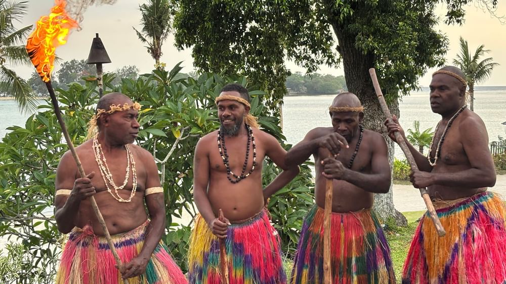 Four men in traditional attire holding torches and sticks at Warwick Le Lagon - Vanuatu, Efate.