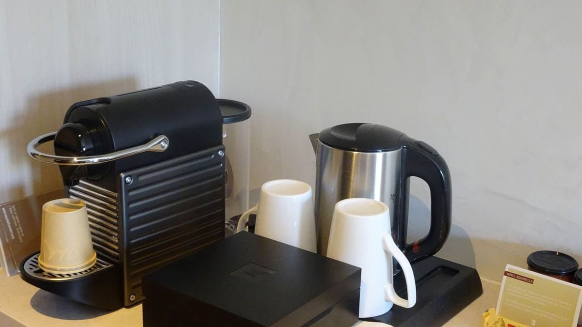 Machine à café, bouilloire, tasses, boîtes et sucreries sur un comptoir blanc.