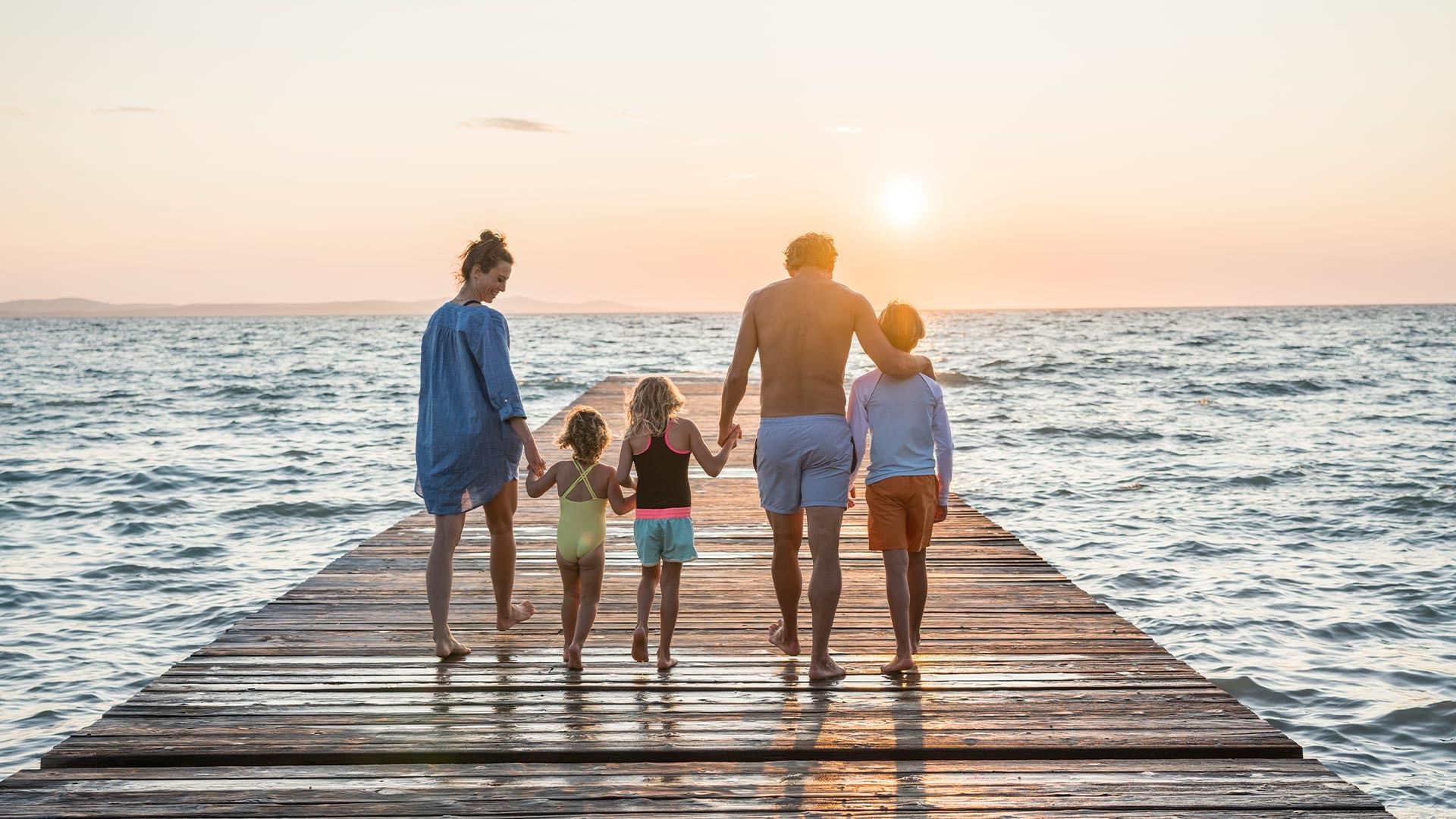 Family walks together on a wooden dock extending into the ocean at sunset.