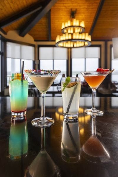Cocktail glasses on a dark bar counter under chandeliers at Rodd Miramichi River, the best places to eat in Miramichi