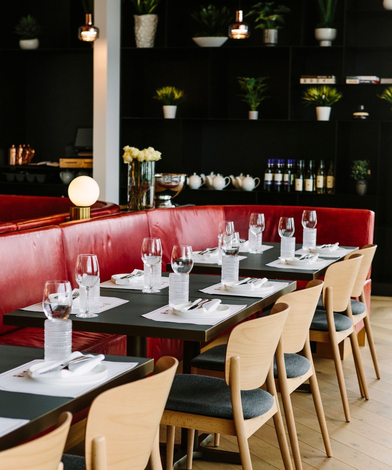 Elegant dining area with red leather banquette, wooden chairs, set tables, and dark display shelves at Hotel X Toronto