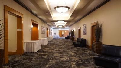 Ballroom hallway with linen-draped tables by meeting room doors, leather chairs under wall art at The Glenmore Inn