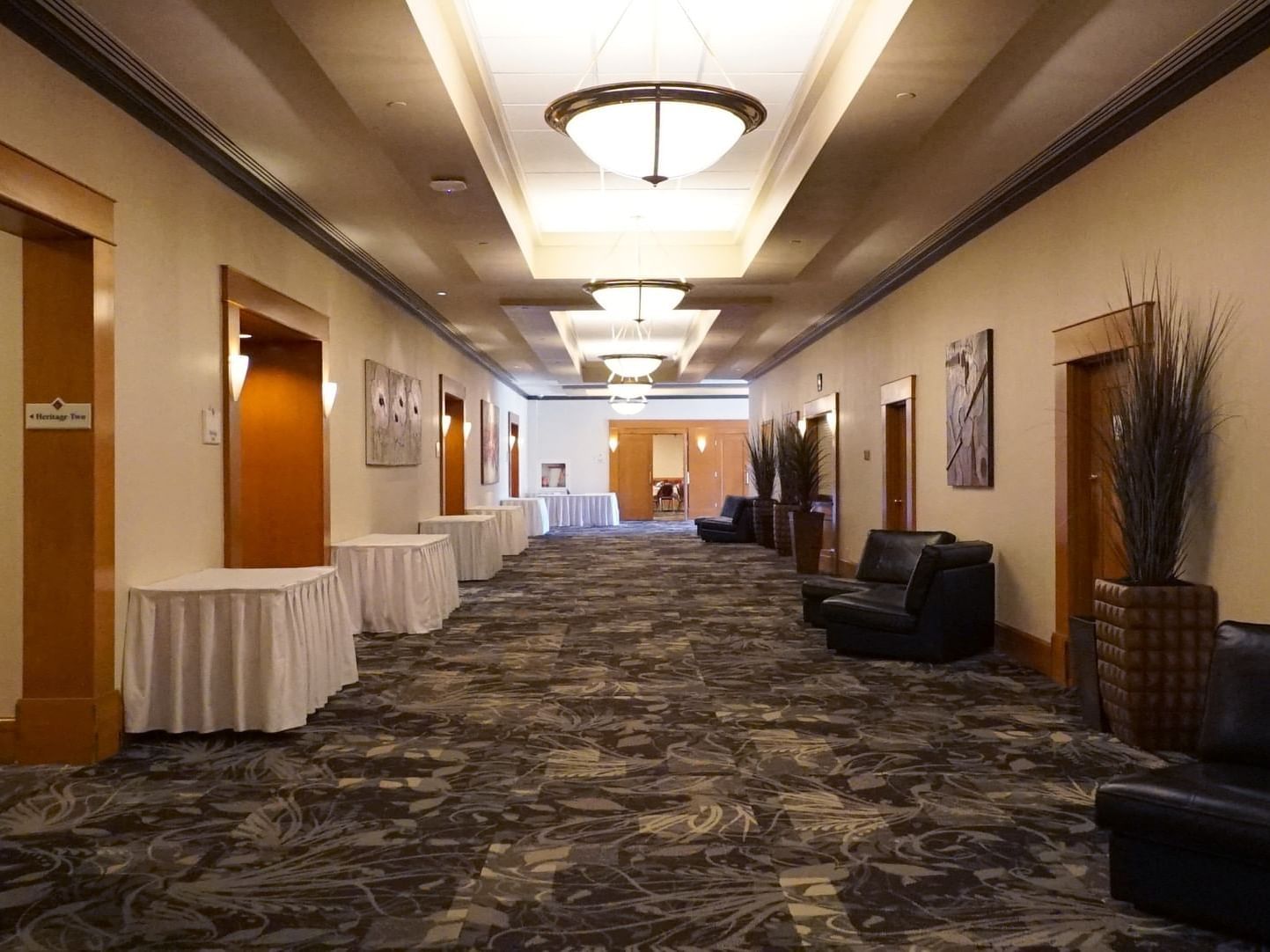 Illuminated ballroom hallway with carpeted floors and table arrangements by doors at The Glenmore Inn & Convention Centre