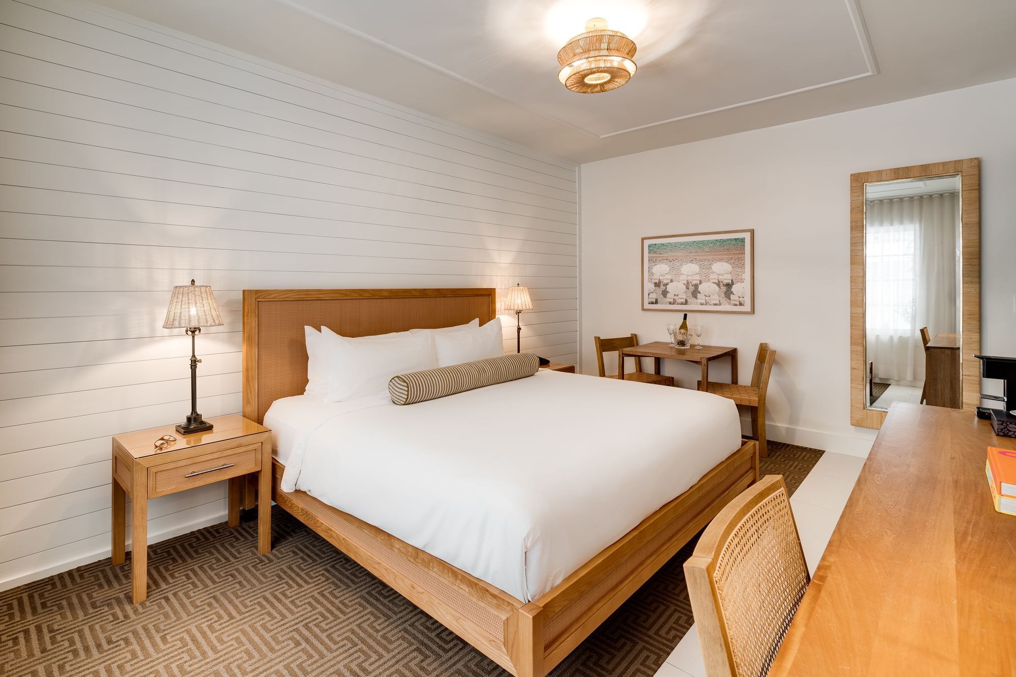 A wide view of a hotel room with a king-sized bed, desk, and mirror