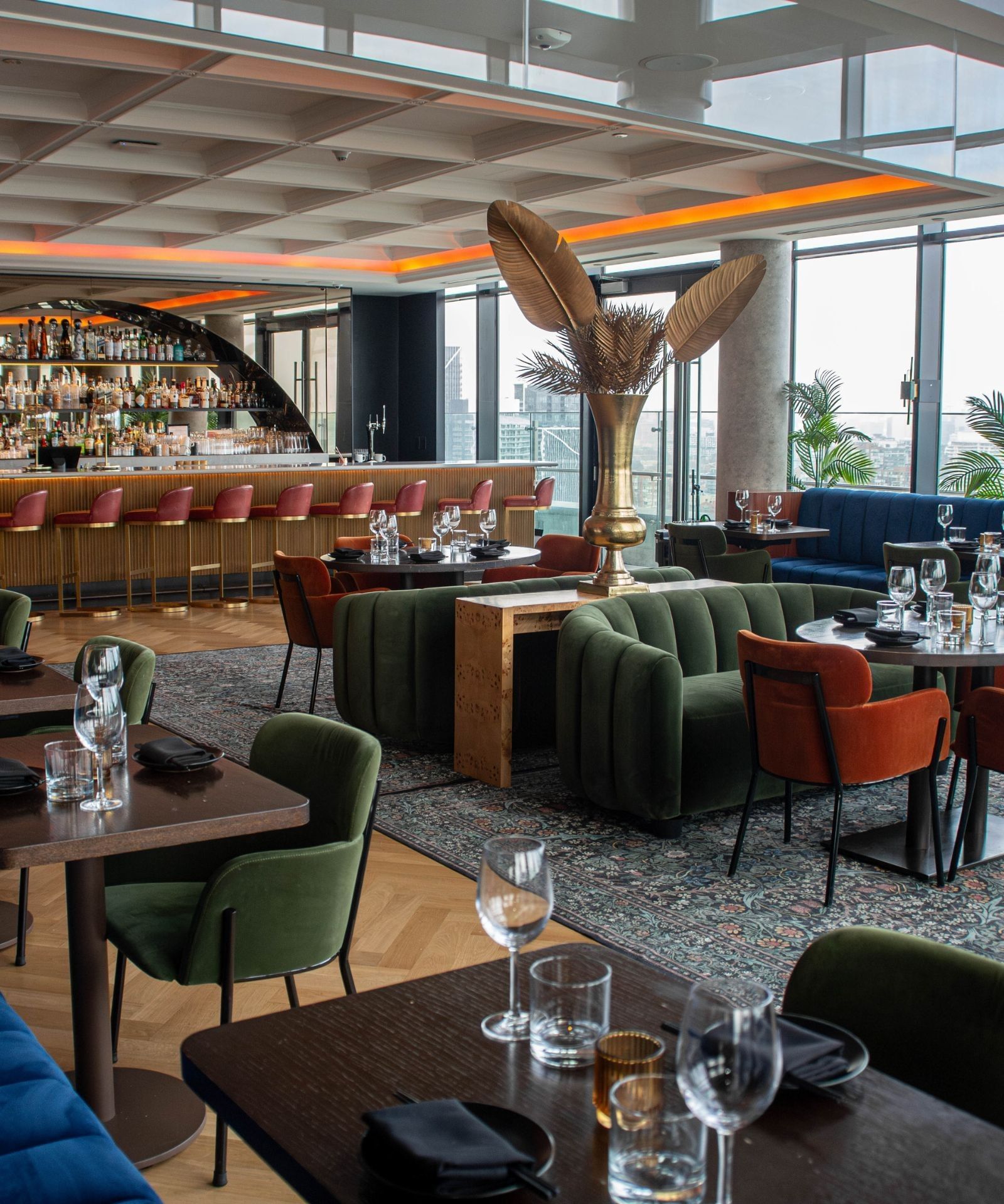 Elegant restaurant with green velvet seating, set dining tables, a curved bar, and wide skyline views at Hotel X Toronto