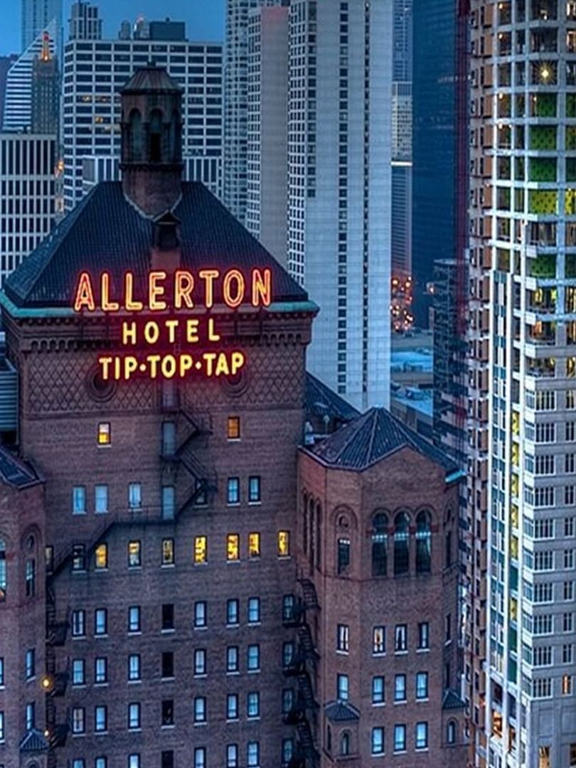 Exterior of the Warwick Allerton Chicago with a glowing sign near city skyscrapers