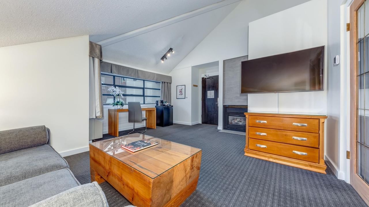 A living room with a couch, coffee table, desk, and a TV mounted on the wall.