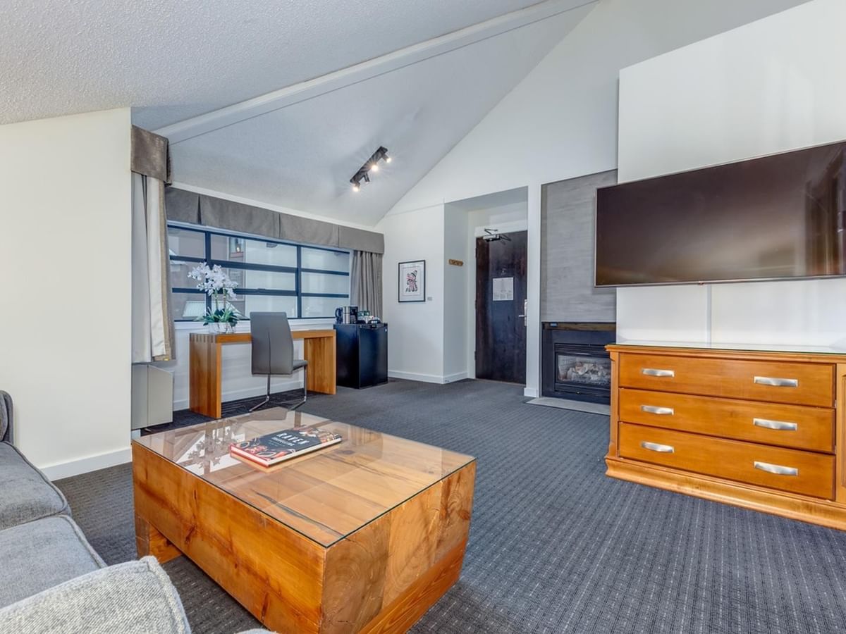 Living room with gray couch, wooden coffee table, desk, dresser, and wall-mounted TV.