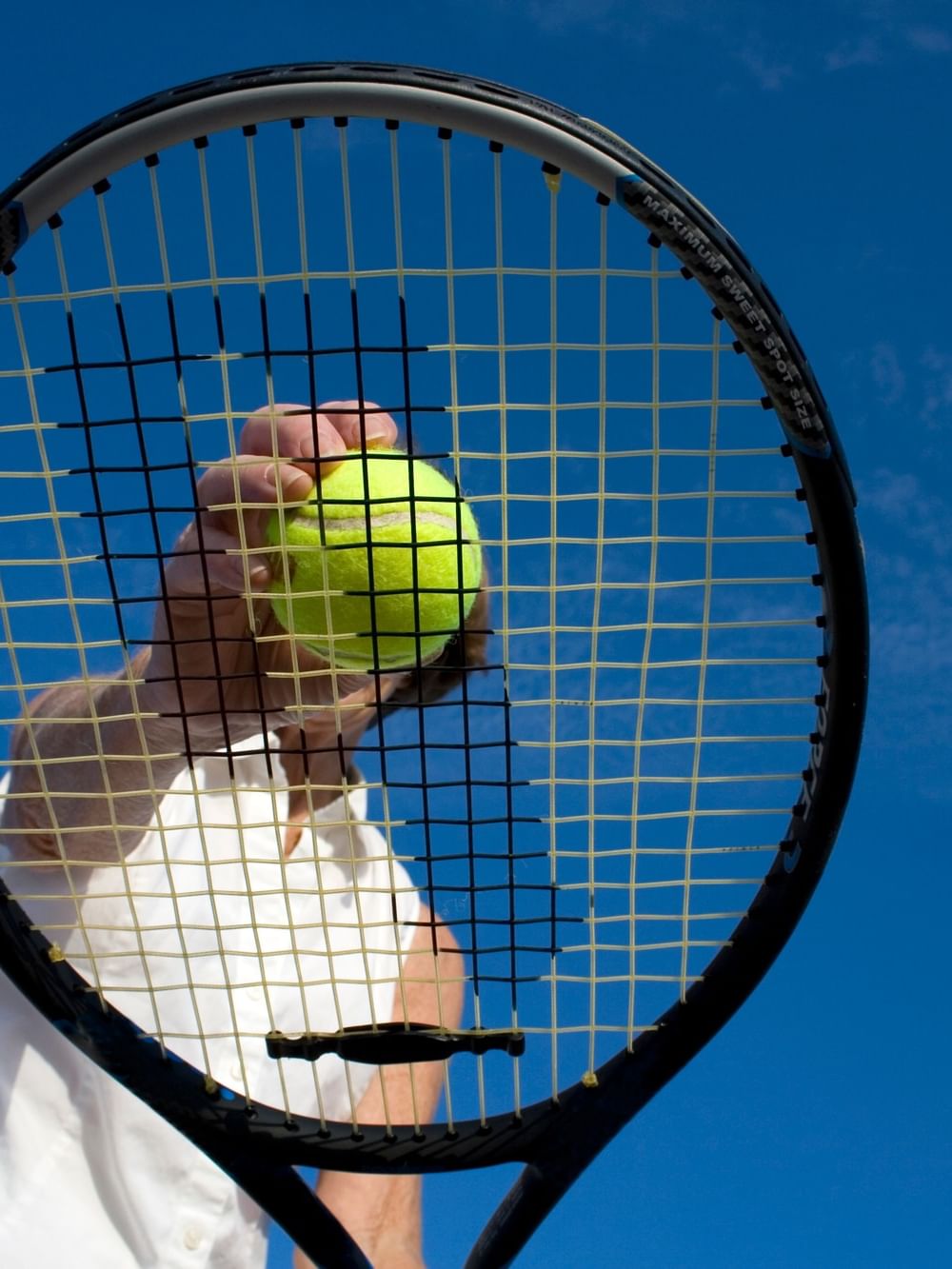 Tennis player holding a yellow ball and racket against a bright blue sky during the US Open Tennis in New York.