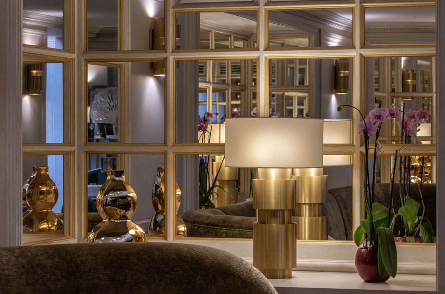 Gold-tiered lamp reflected in paneled mirrors beside orchids at the Hotel Barsey by Warwick