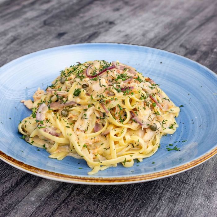 A blue plate filled with creamy pasta, topped with herbs and onions, on a wooden table.