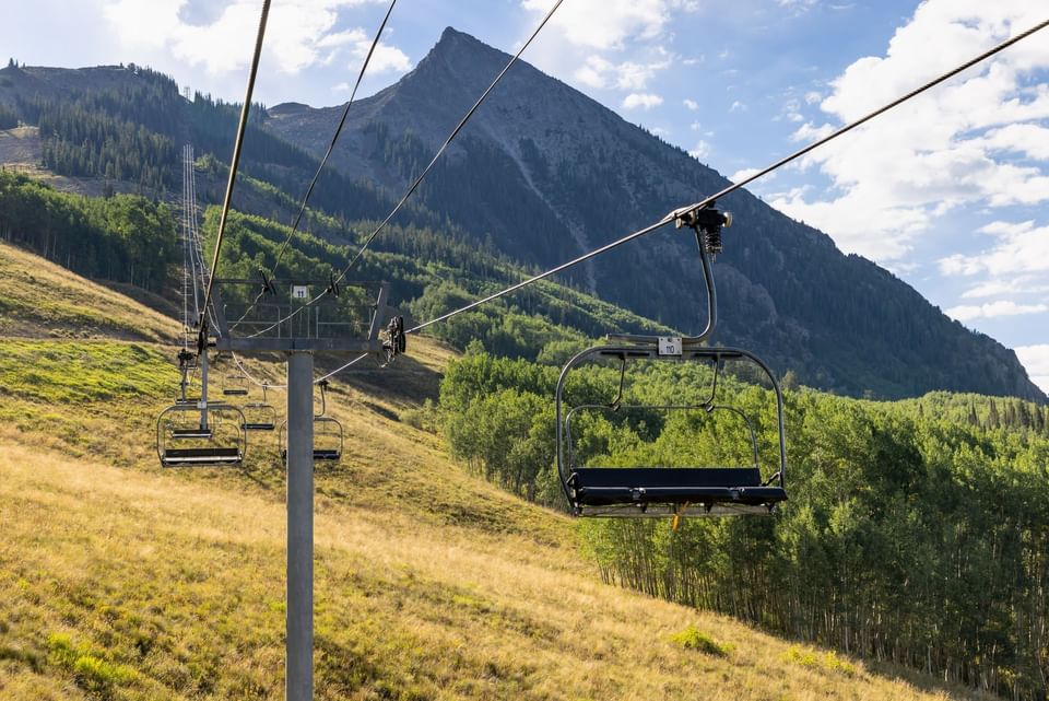 Ski lift with two empty chairs suspended above grassy slope and mountain range at Elevation Resort Spa