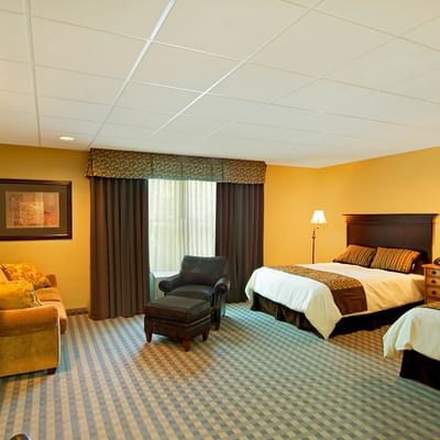 A well-lit hotel room with two beds, a small sofa, and a comfortable armchair at The Pointe at Castle Hill