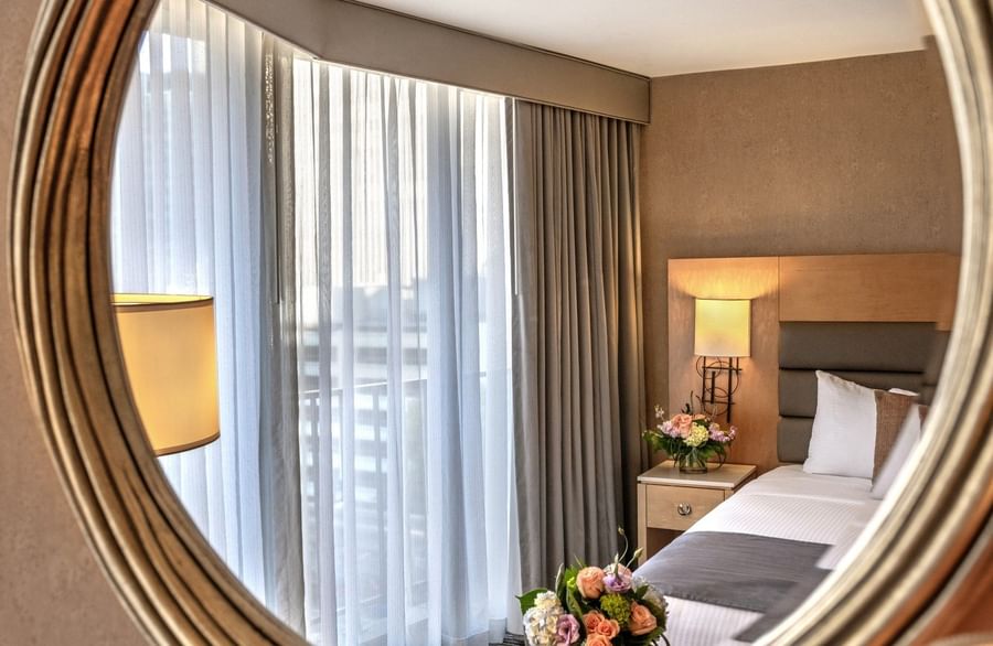 Circular mirror by a bed and flowers reflecting a window with sheer drapes in Executive Room at Warwick Seattle