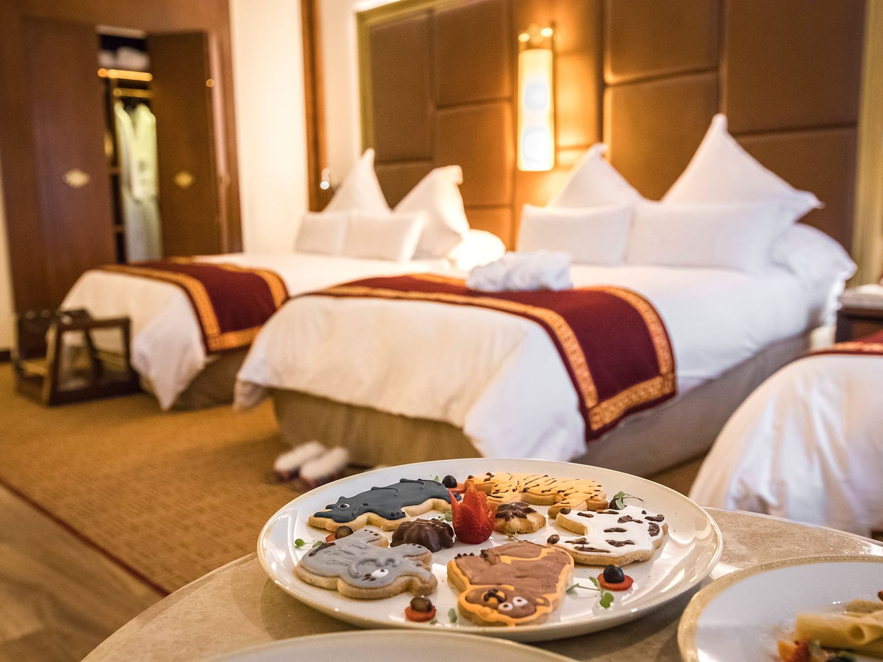 Spacious family room with two beds dressed in white linens and burgundy runners, featuring a dessert platter at Sumaq Machu Picchu Hotel.