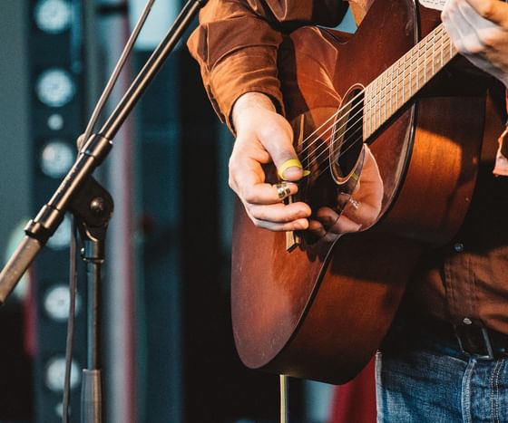 Musician playing a brown acoustic guitar by a microphone under stage lights at Paramount Hotel Seattle