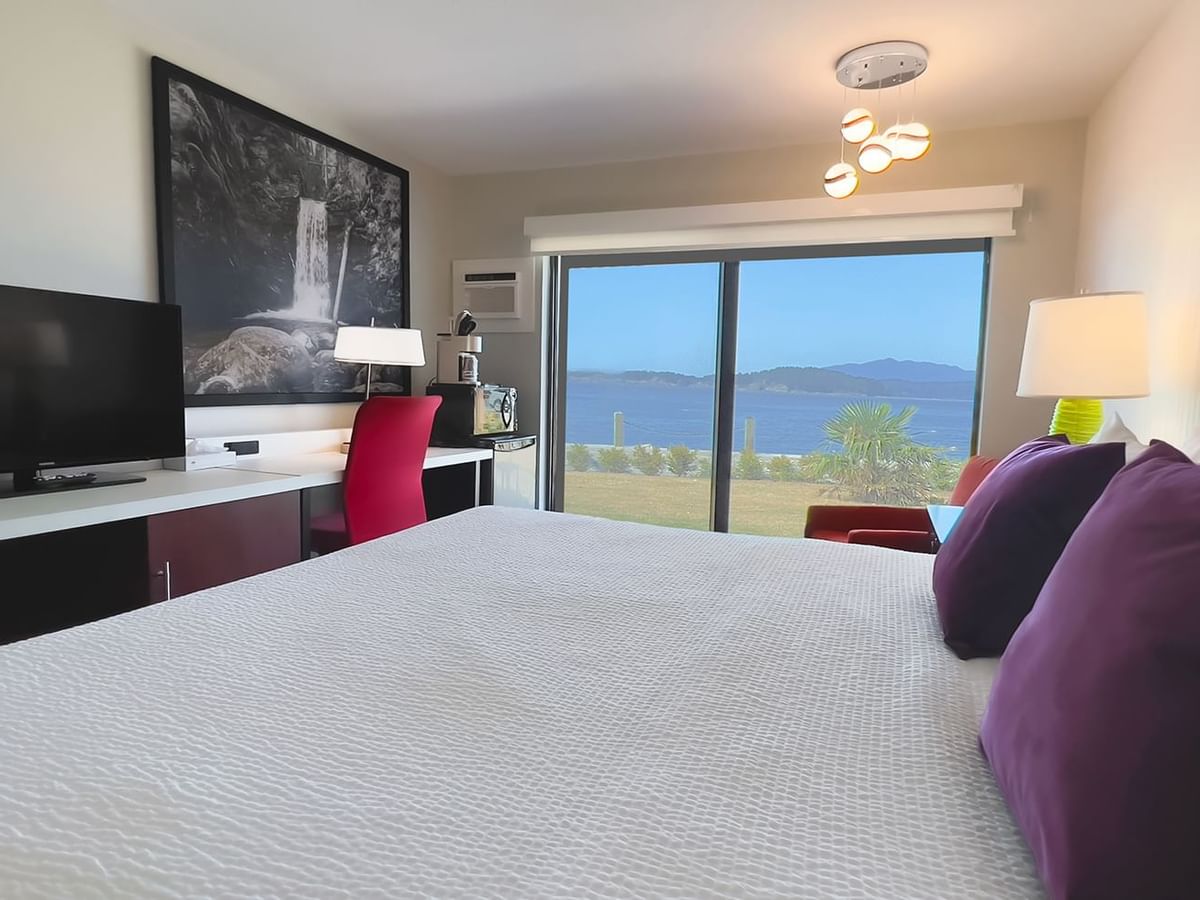 Guest room with king bed, lamps, tv, patio doors, red chair, desk, desk chair, microwave, fridge