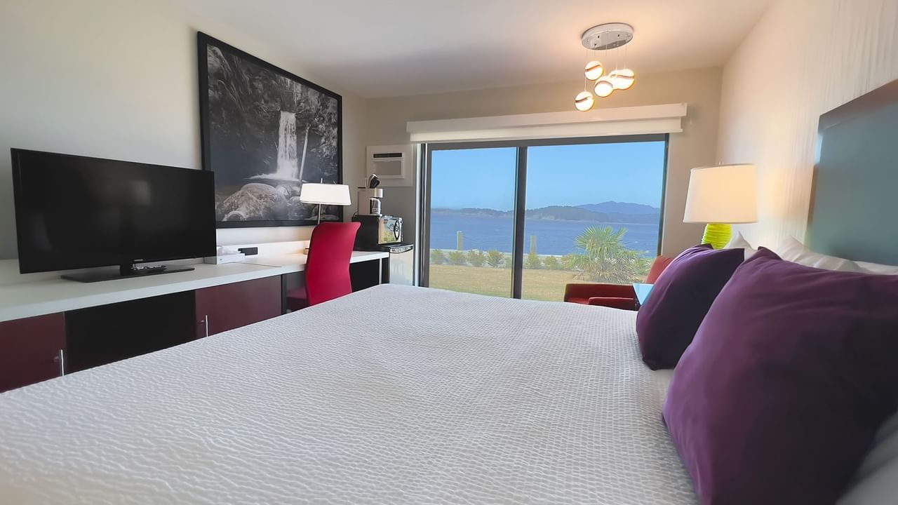 Guest room with king bed, lamps, tv, patio doors, red chair, desk, desk chair, microwave, fridge