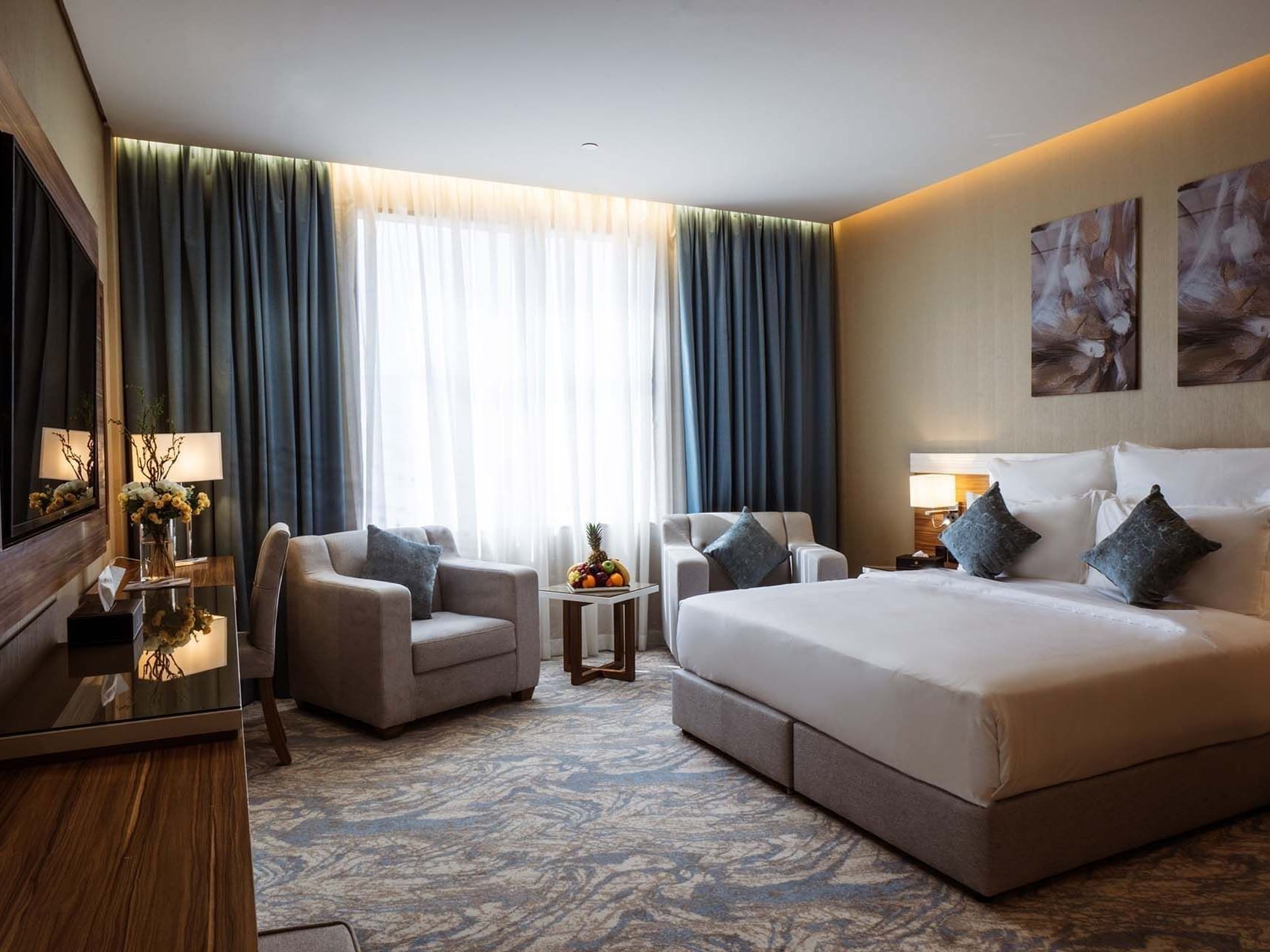 Large bed with armchairs by a fruit tray under a large window in Standard King Room at Cantonal Hotel by Warwick Riyadh