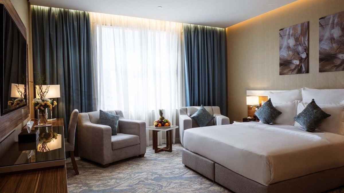 Large bed with armchairs by a fruit tray under a large window in Standard King Room at Cantonal Hotel by Warwick Riyadh