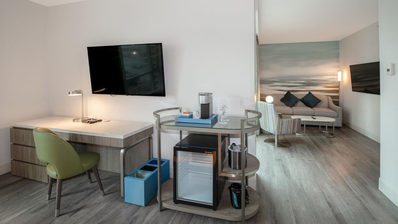 Modern hotel room with desk, chair, mini-fridge, and couch.
