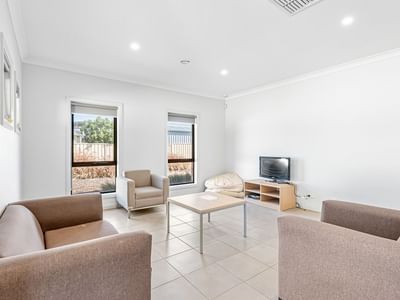 Light living room with sofa, chairs, TV, and table at La Trobe University Regional Housing – Mildura.