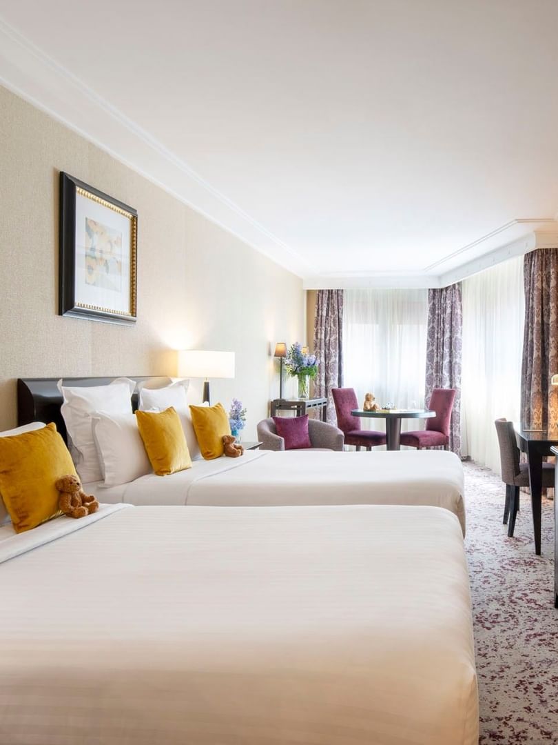 Twin beds by a TV console under framed artwork in Family room with two queen beds at Warwick Paris Champs Elysées