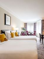 Twin beds by a TV console under framed artwork in Family room with two queen beds at Warwick Paris Champs Elysées