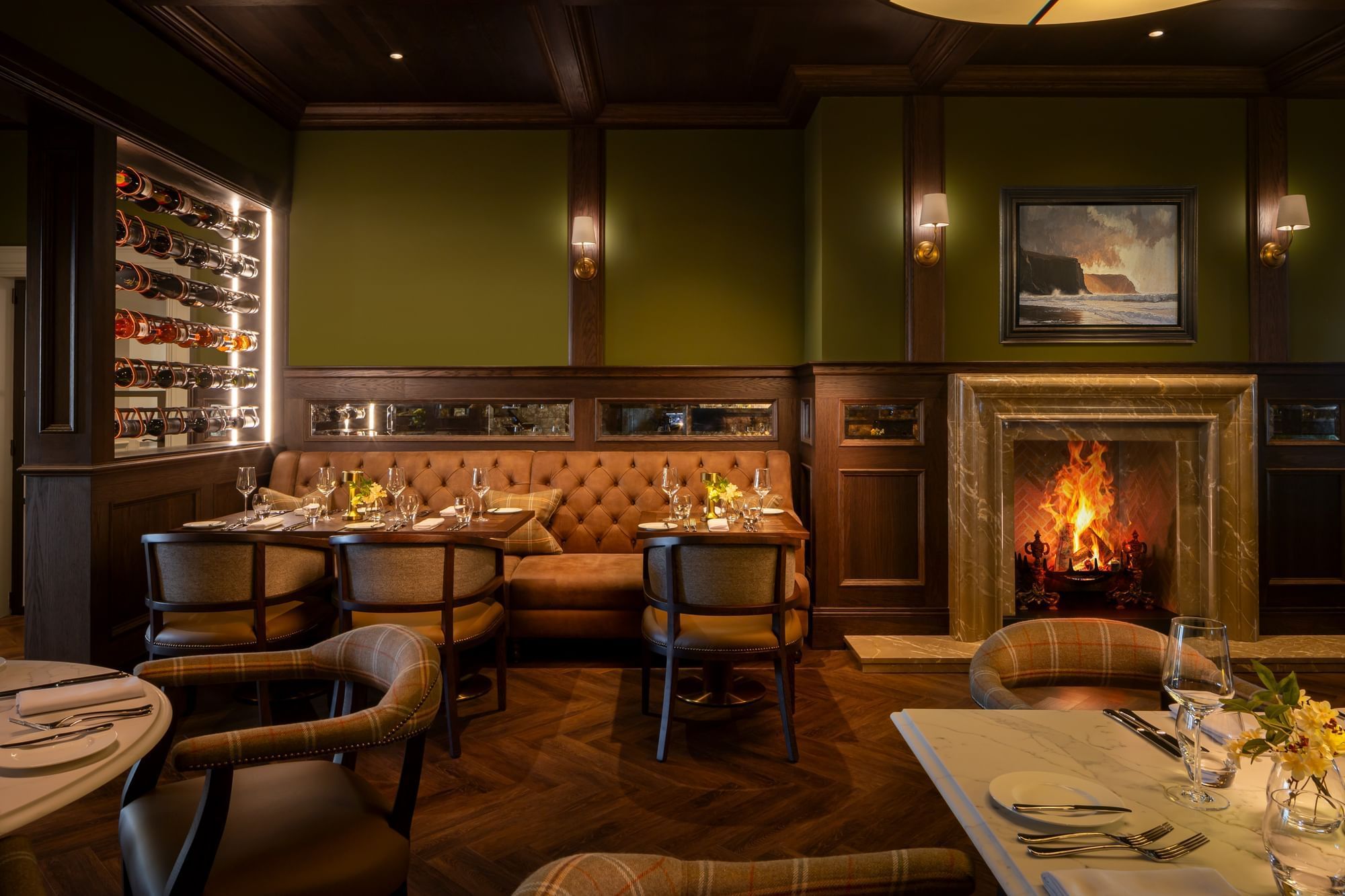 A cozy restaurant nook with a tufted sofa, glowing fireplace, and full wine rack at Dunluce Lodge