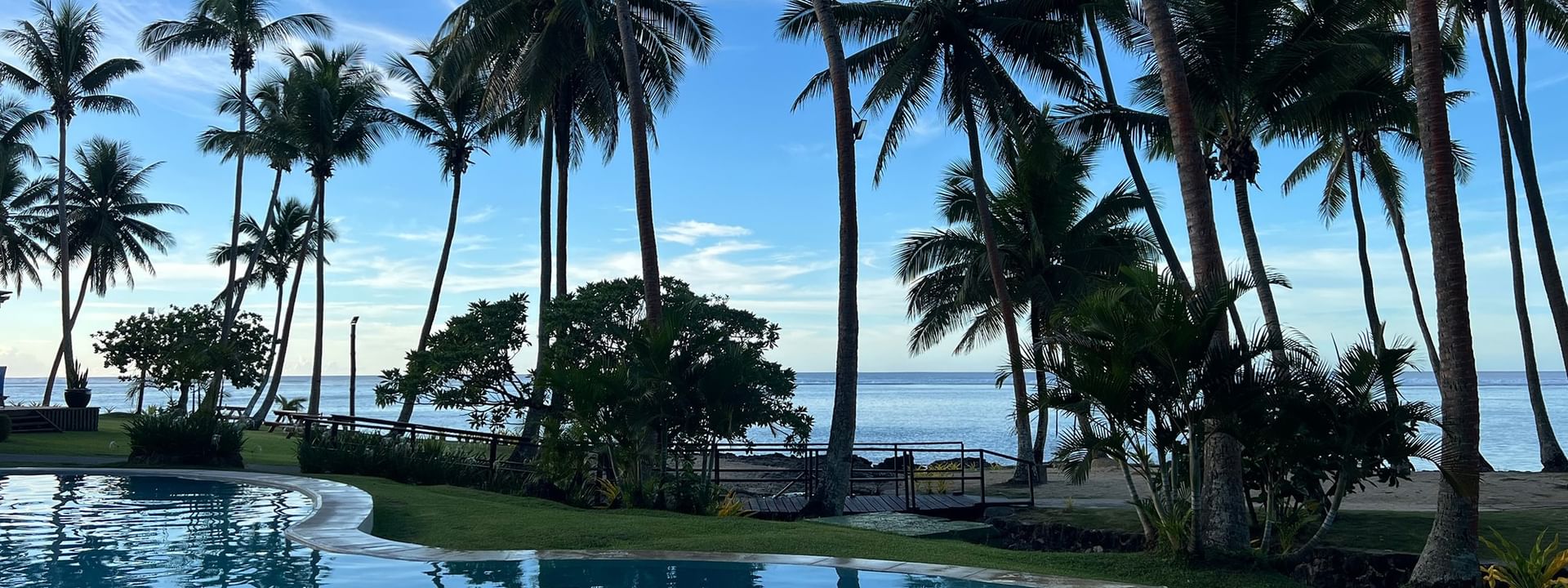Clear pool with palm trees and ocean view at Tambua Sands Beach Resort in Sigatoka
