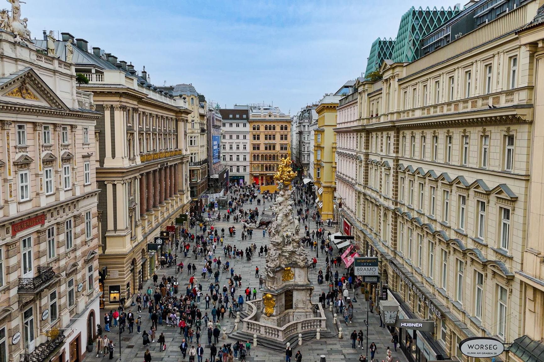 Der Graben in Wien mit der barocken Pestsäule, umgeben von historischen Gebäuden und zahlreichen Menschen im Stadtzentrum.
