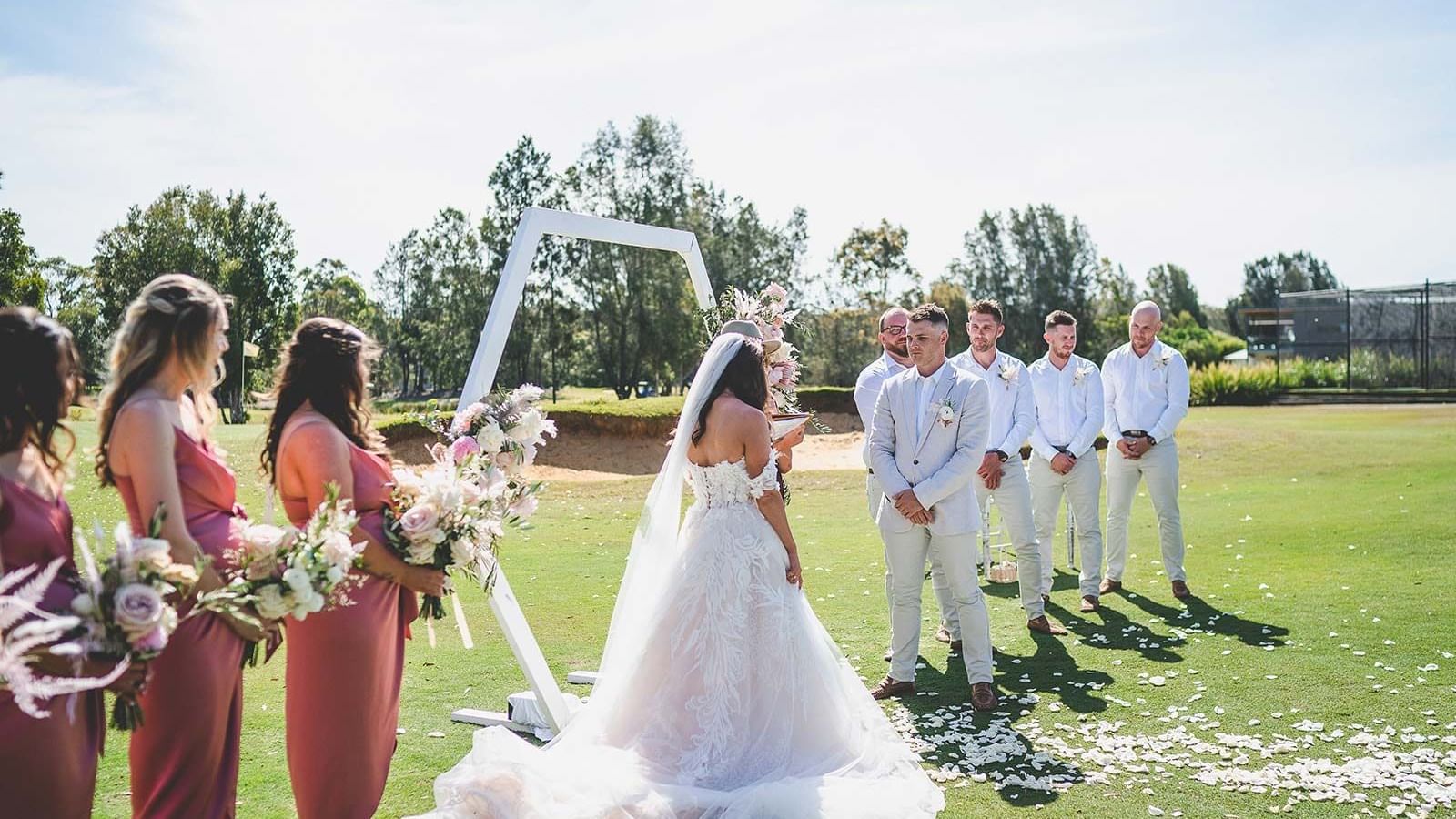 Outdoor wedding scene with bride, groom, and bridesmaids with groomsmen at Mercure Kooindah Waters