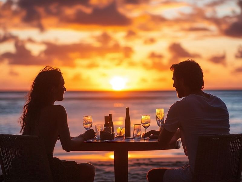 Silueta de pareja disfrutando cena romántica con velas en la playa de Fiesta Americana Funeeq al atardecer