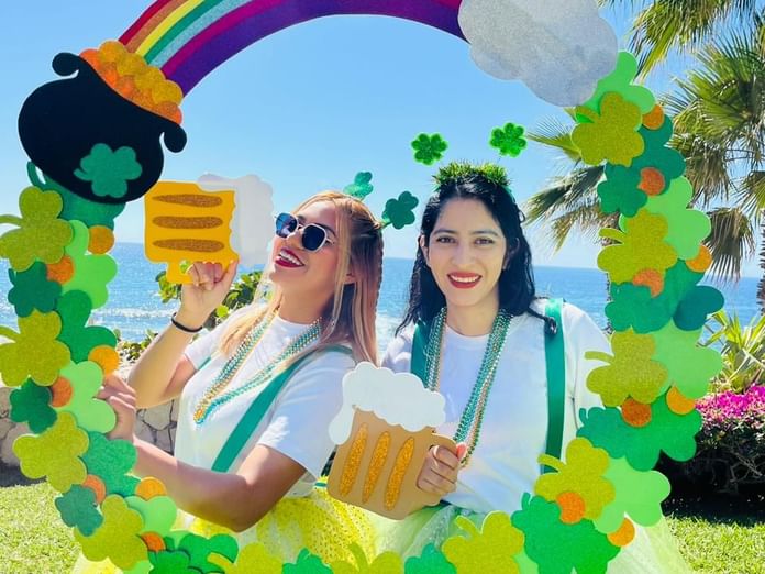 Dos mujeres sonrientes celebrando el Día de San Patricio en una vibrante cabina de fotos en Hacienda del Mar Los Cabos