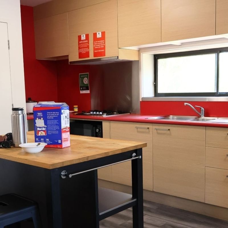 Modern kitchen with red counters, wooden cabinets, and appliances at La Trobe University Hillside Apartments.
