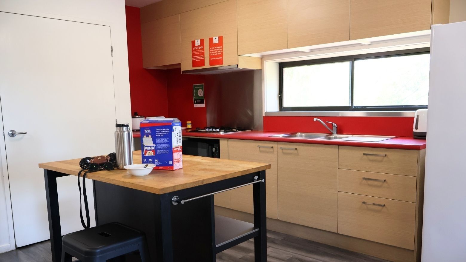 Modern kitchen with red counters, wooden cabinets, and appliances at La Trobe University Hillside Apartments.