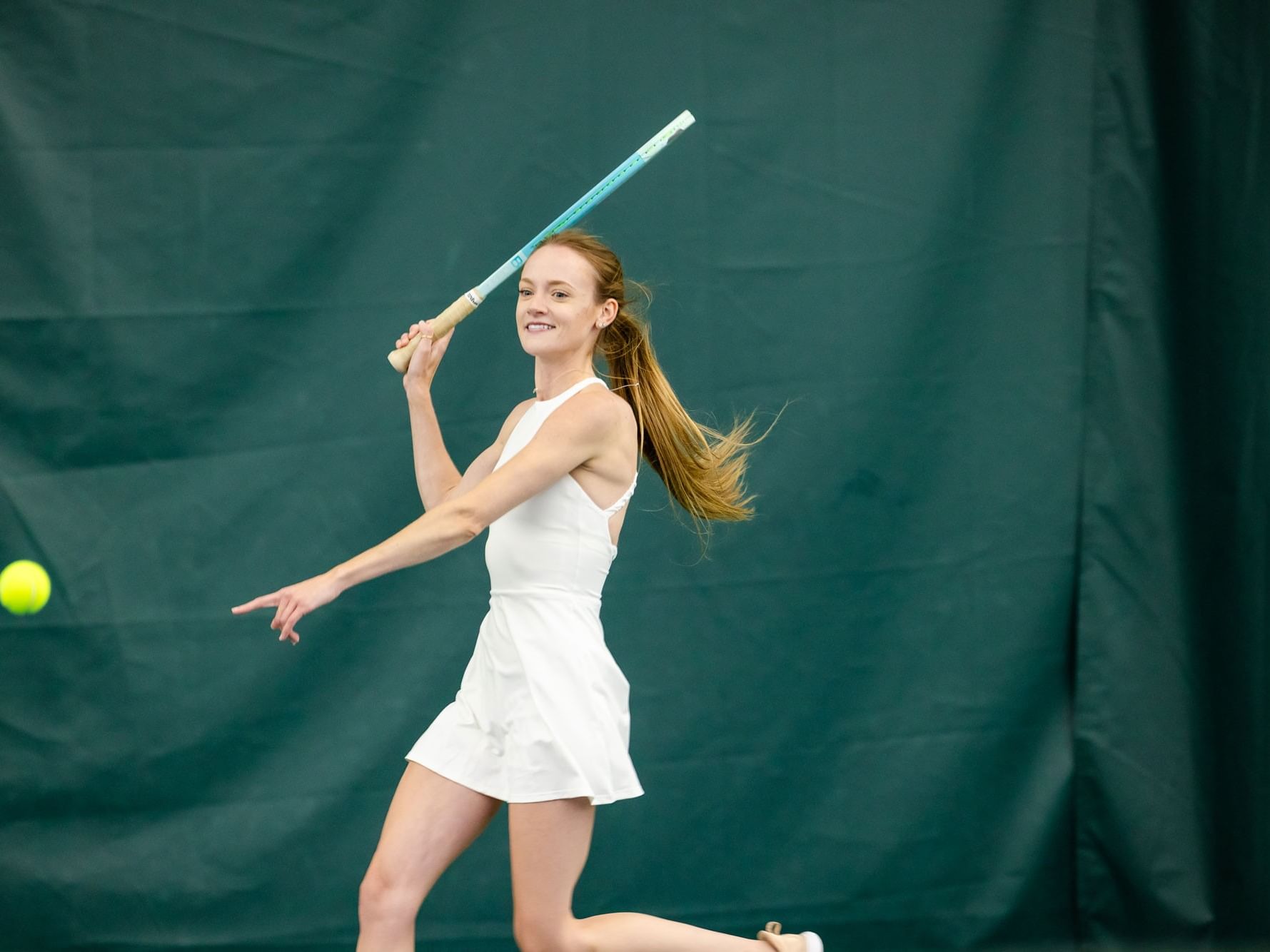 Woman in white tennis dress hitting a ball with racket on court during 3.5+ Point Play Clinic.