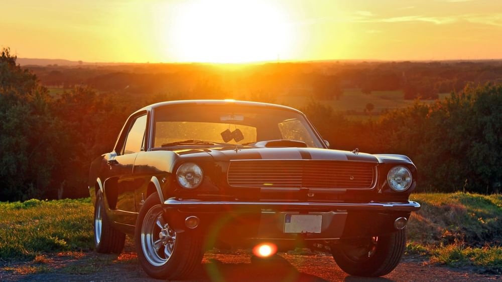 Classic black car parked by a grassy field under a bright setting sun near Warwick Grand Place Brussels