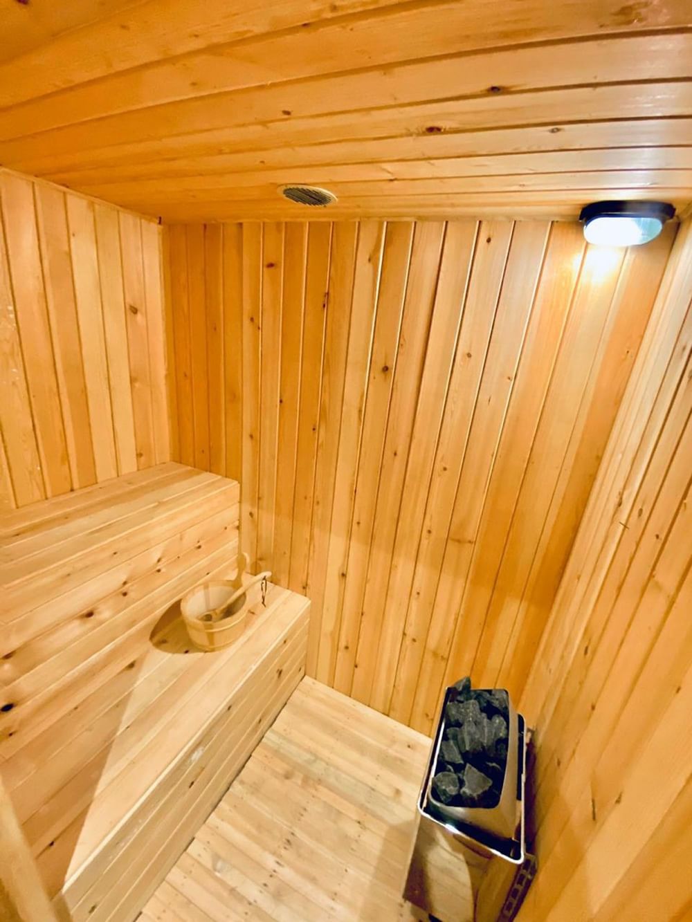 Gold Spa Sauna room, featuring a wooden bucket with a ladle, with layered benches at Naviti By Warwick Dammam