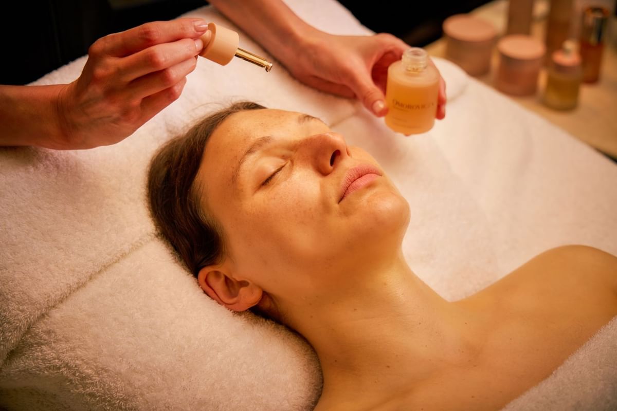 Lady lies on a massage table as facial oil is gently applied with a dropper at The May Fair Spa, The May Fair Hotel