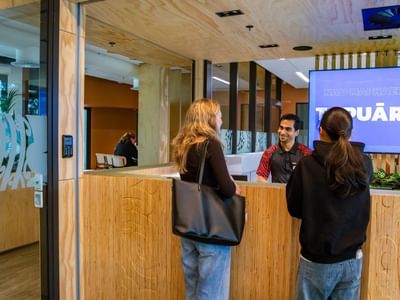 Guests checking in at a modern wooden reception desk with staff member in contemporary hotel lobby featuring Tupuārangi signage