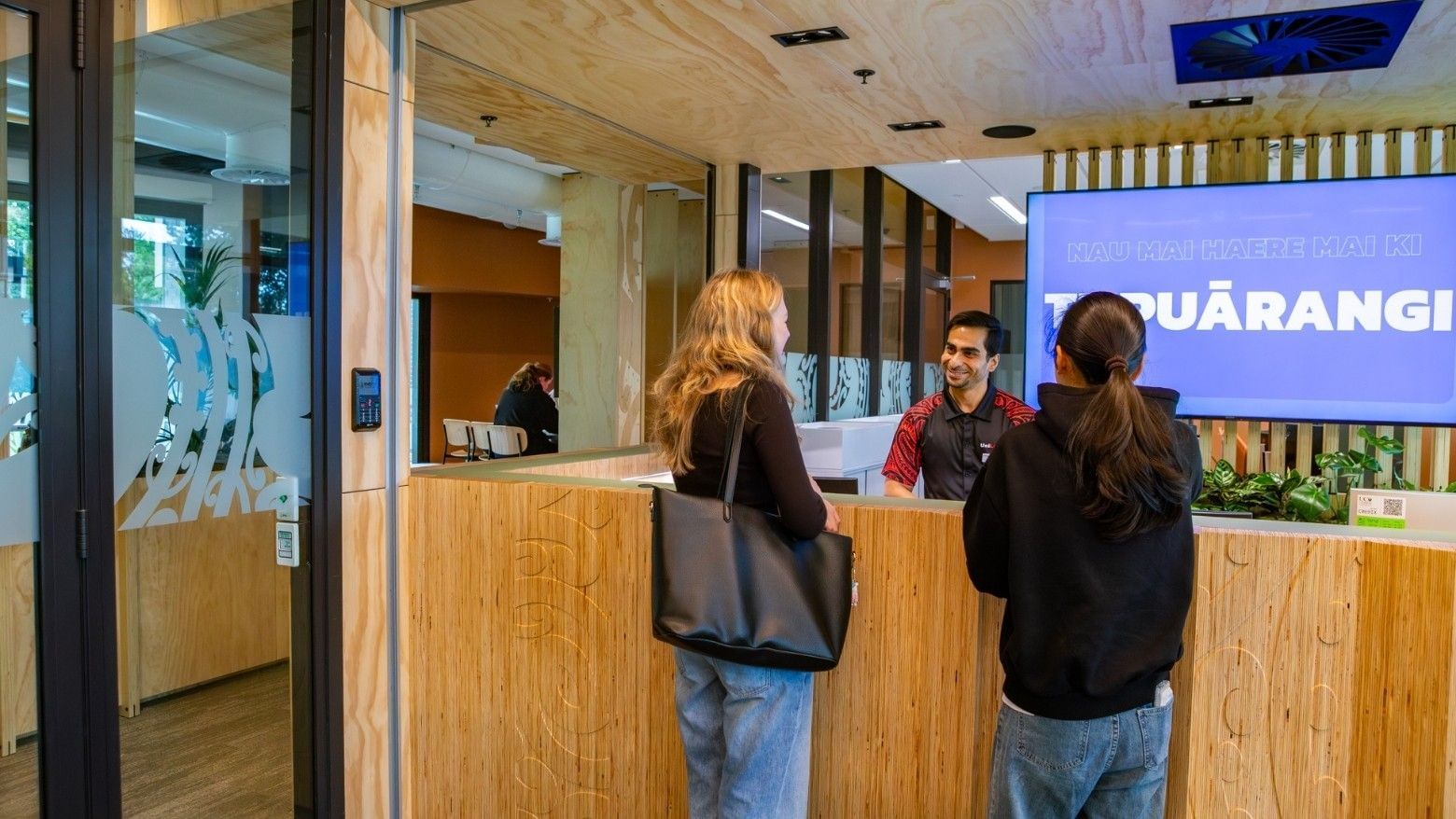 Guests checking in at a modern wooden reception desk with staff member in contemporary hotel lobby featuring Tupuārangi signage