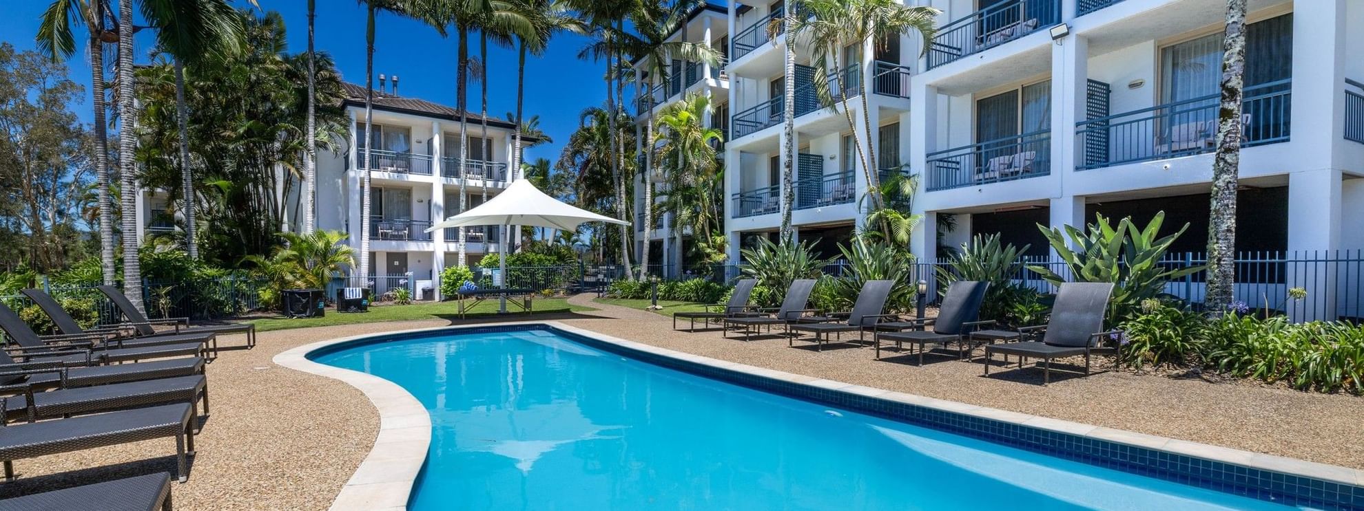 The Billabong Pool surrounded by lounge chairs and lush greenery at Mercure Gold Coast Resort in Carrara.